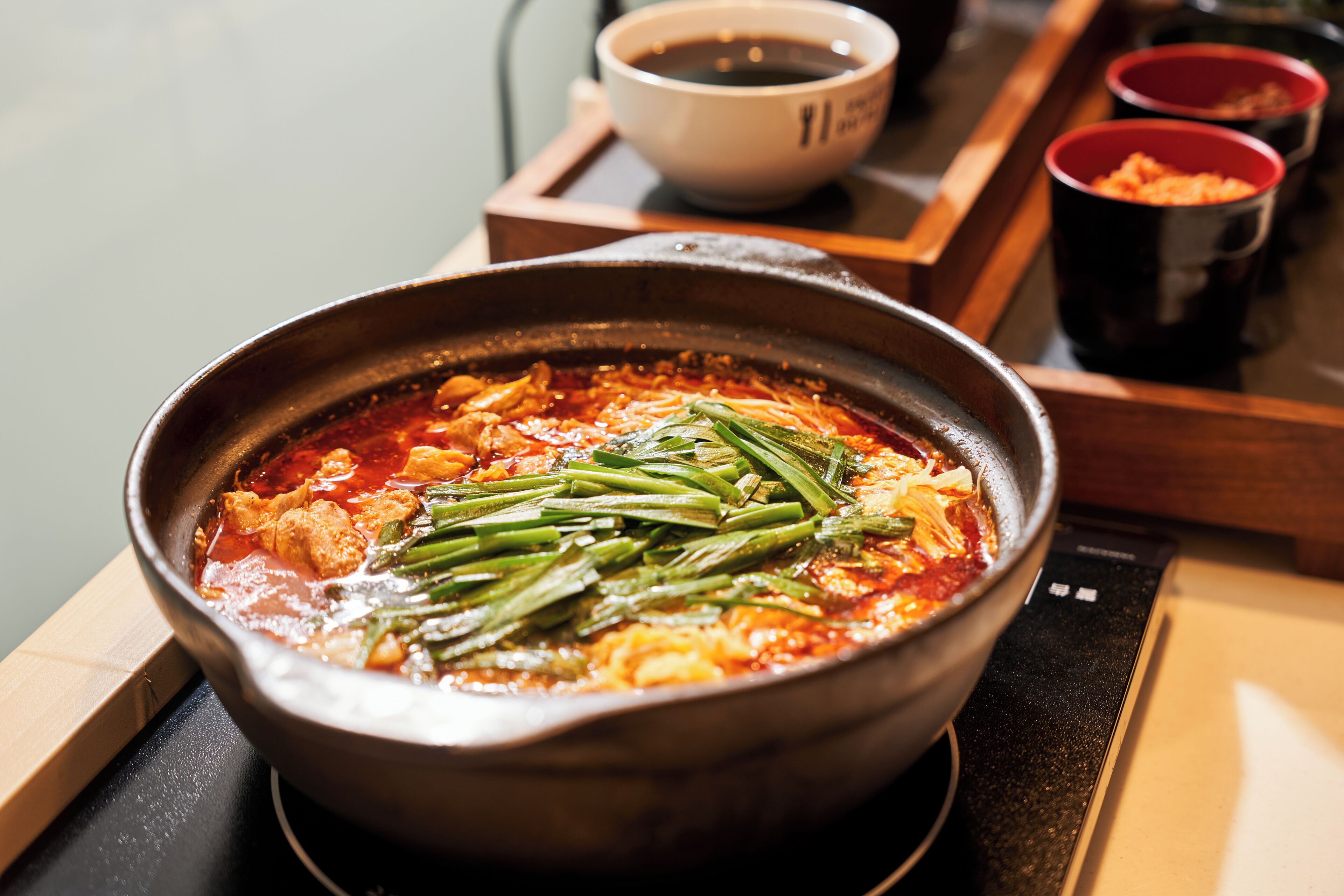A bowl of soup with vegetables and meat, a cup of coffee, and a wooden tray with a bowl and a cup.
