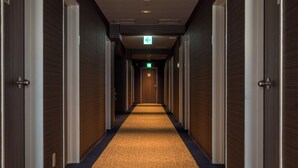 Un pasillo de hotel con puertas de madera, piso alfombrado y letrero de salida.