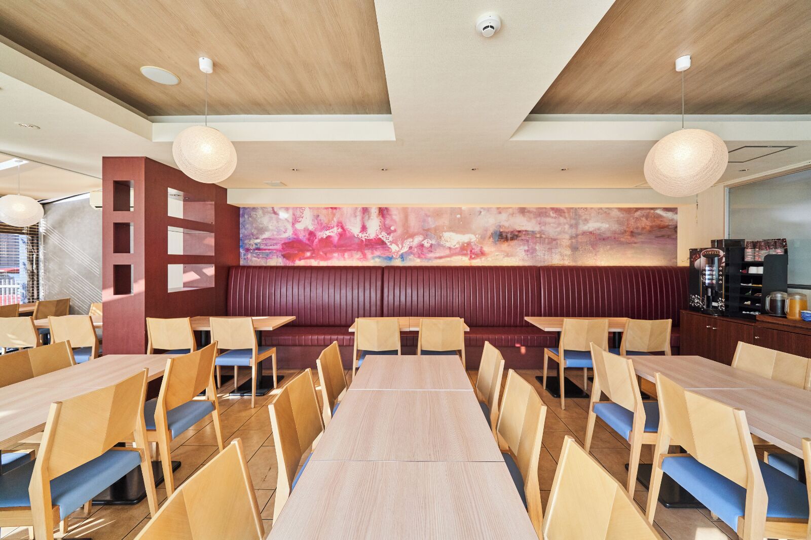 Un restaurant avec une longue table en bois, plusieurs banquettes et un grand tableau abstrait accroché au mur.