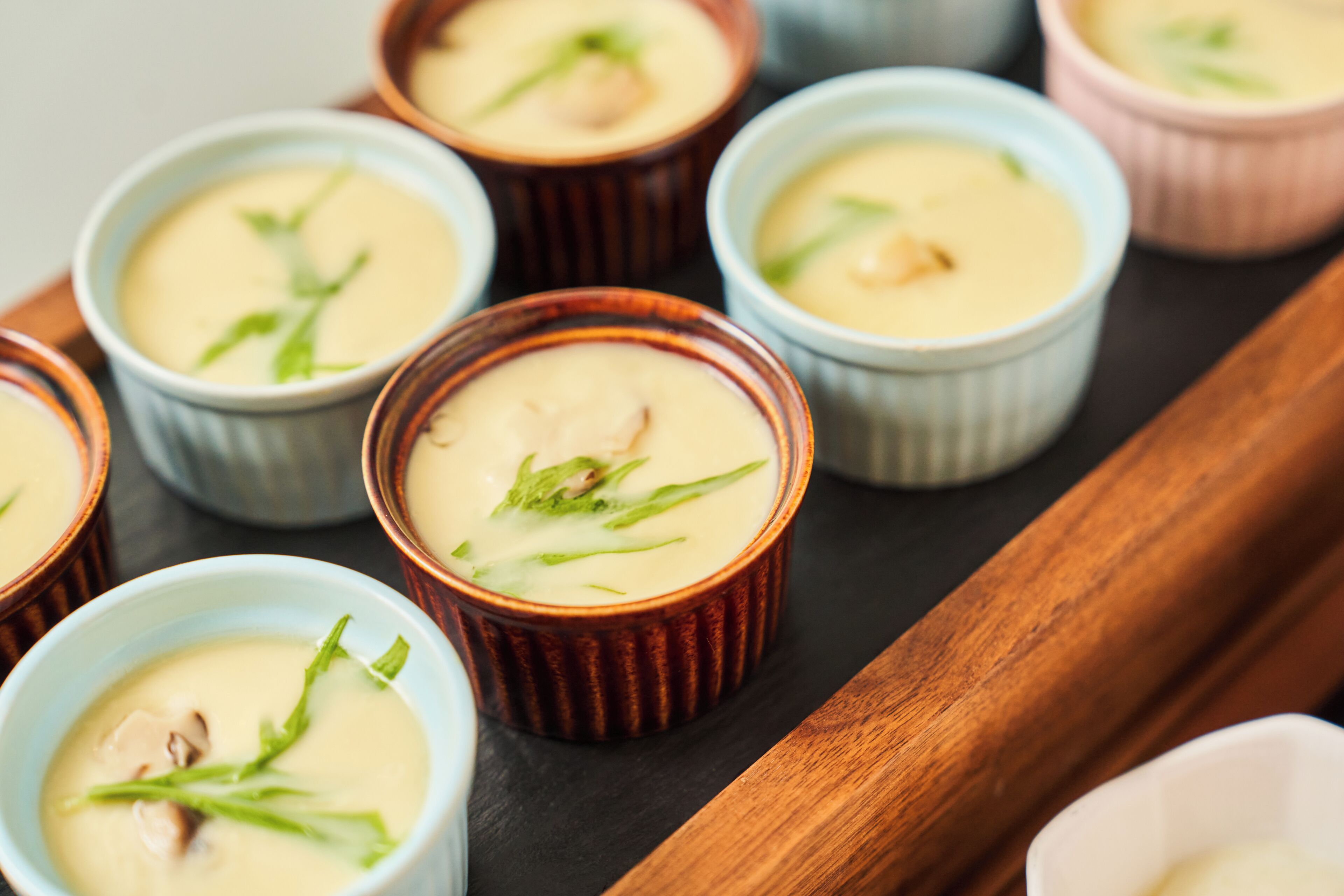 A tray with several small bowls of creamy soup garnished with green leaves.