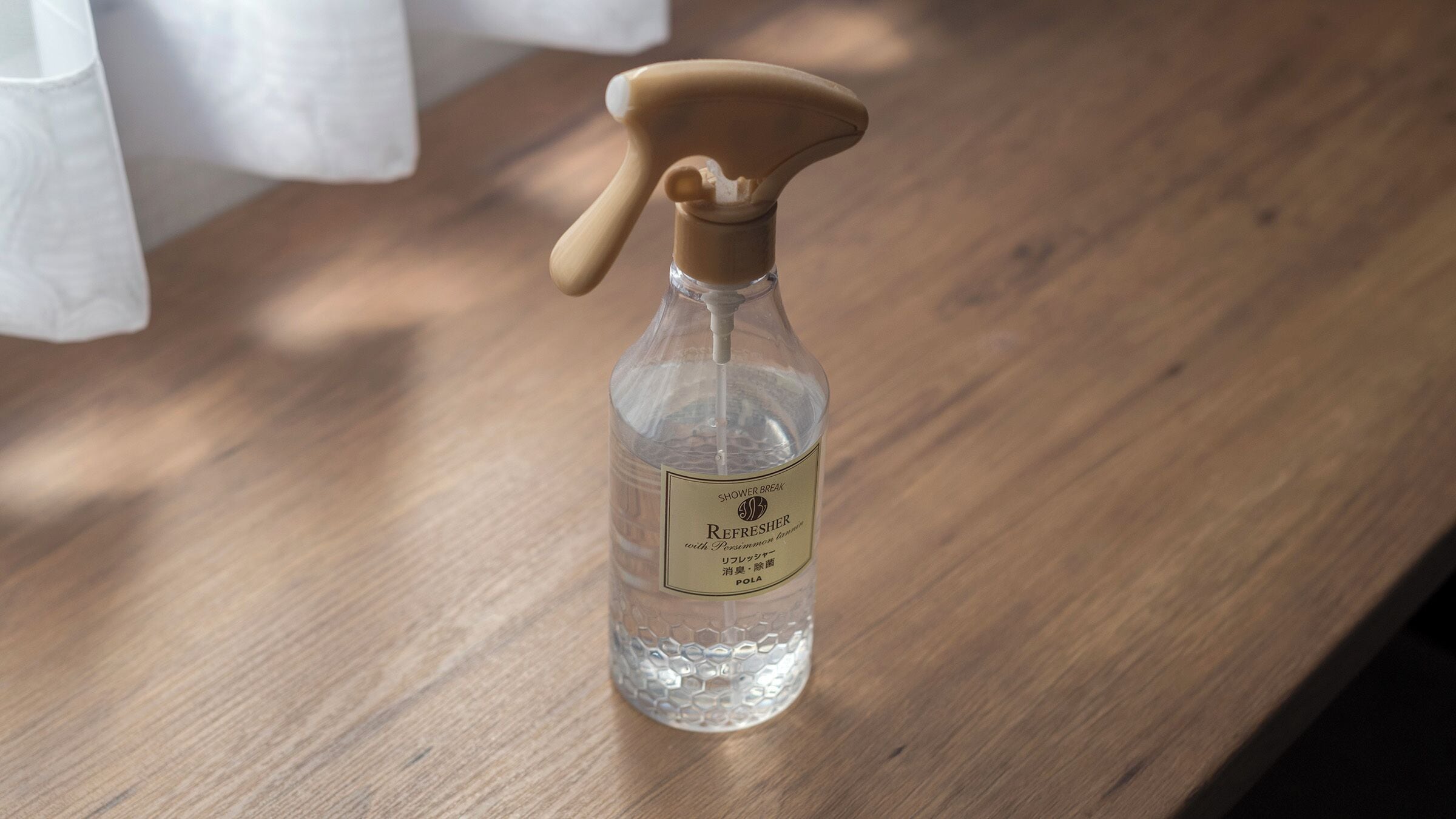 Una botella de vidrio transparente con un atomizador y una etiqueta sobre una superficie de madera.