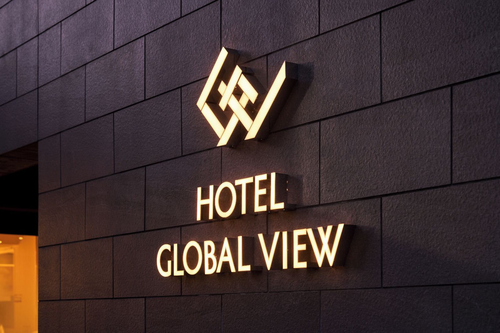 Une enseigne d’hôtel avec un logo géométrique et l’inscription « HOTEL GLOBAL VIEW » sur un mur sombre.
