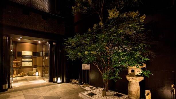 A hotel entrance with a stone lantern, a small tree, and a sign indicating the hotel name.