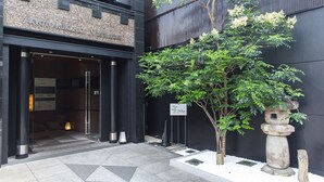 A building entrance with a stone pillar, a sign, and a tree.