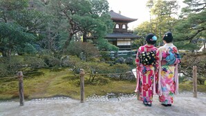 Two individuals in traditional attire standing in a garden with a pagoda in the background.