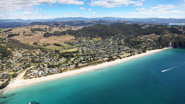 An aerial view of a coastal town with a beach, houses, and a boat in the water. - Tatahi Lodge Beach Resort (Hahei)