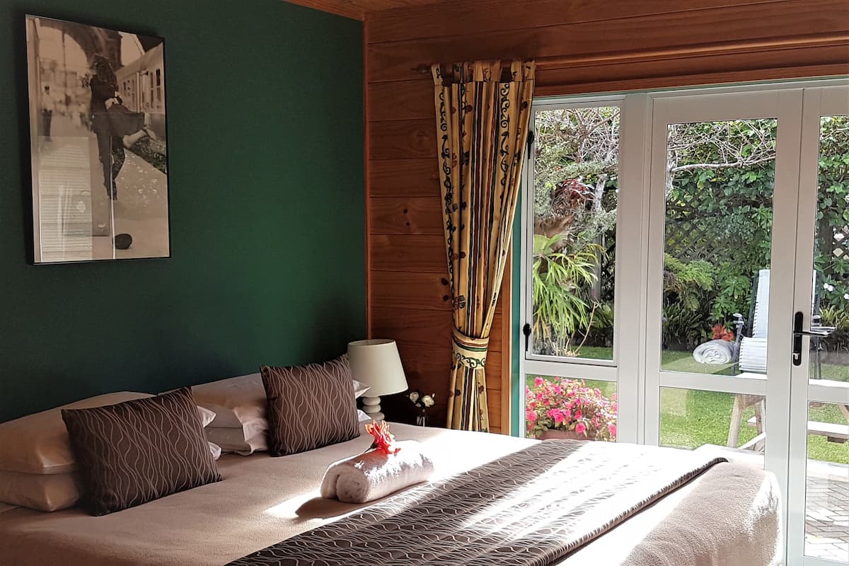 A bedroom with a bed, pillows, a lamp, and a view of a garden through a glass door.