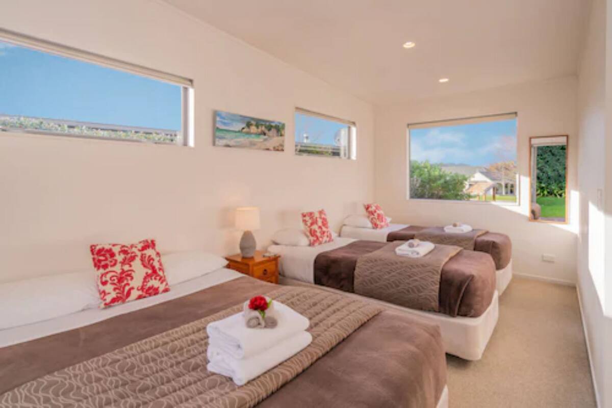 A hotel room with two beds, a small table, and a window with a view of the sea.