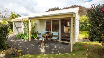 A covered patio with a table and chairs, surrounded by a garden with various plants and a lawn.