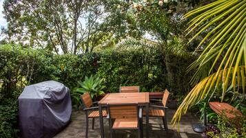 An outdoor patio with a covered table and chairs, surrounded by lush greenery and a palm tree.