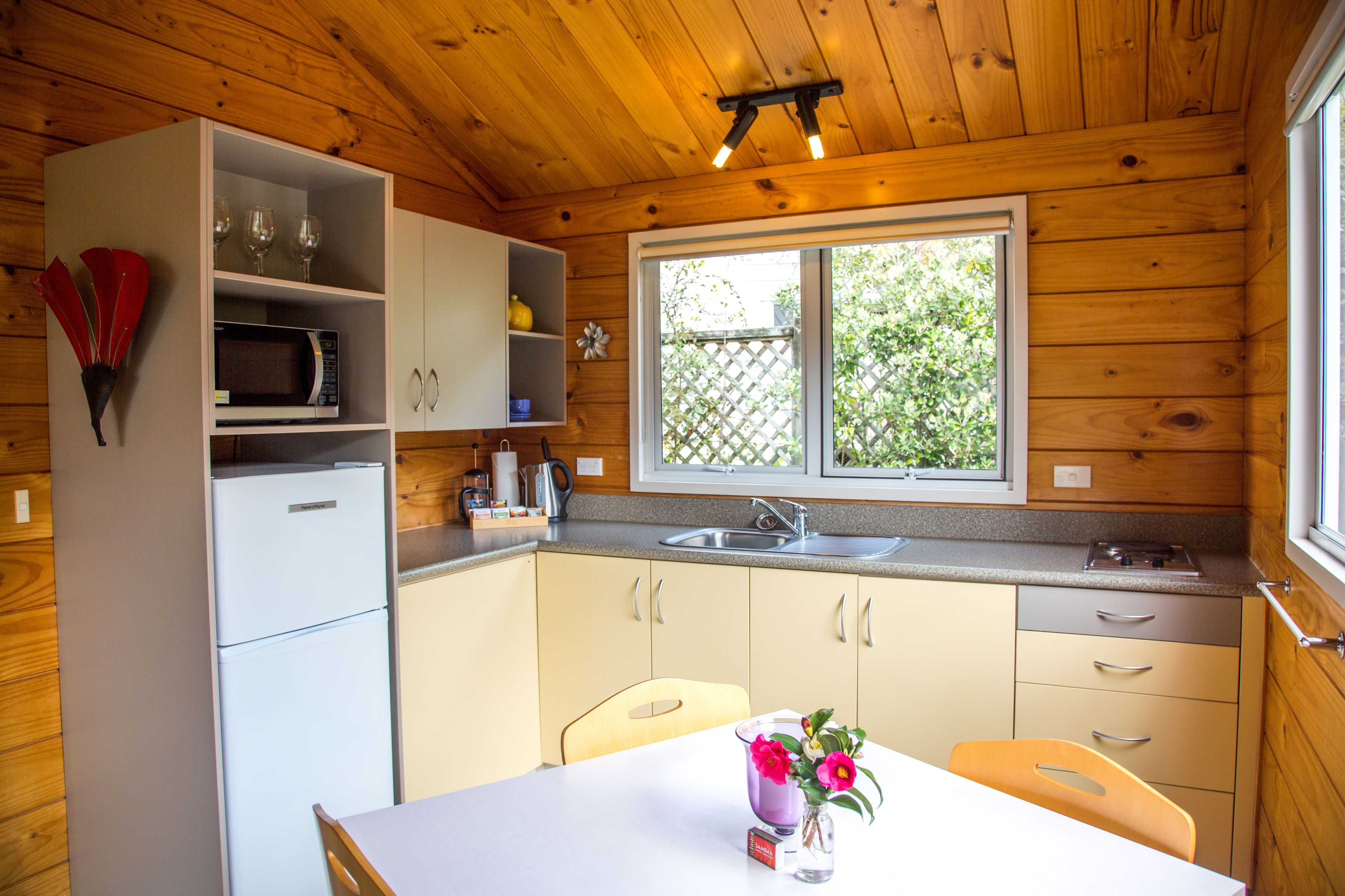Une cuisine compacte équipée d’un four à micro-ondes, d’un évier et de meubles en bois. Une fenêtre offre une vue sur la verdure environnante.