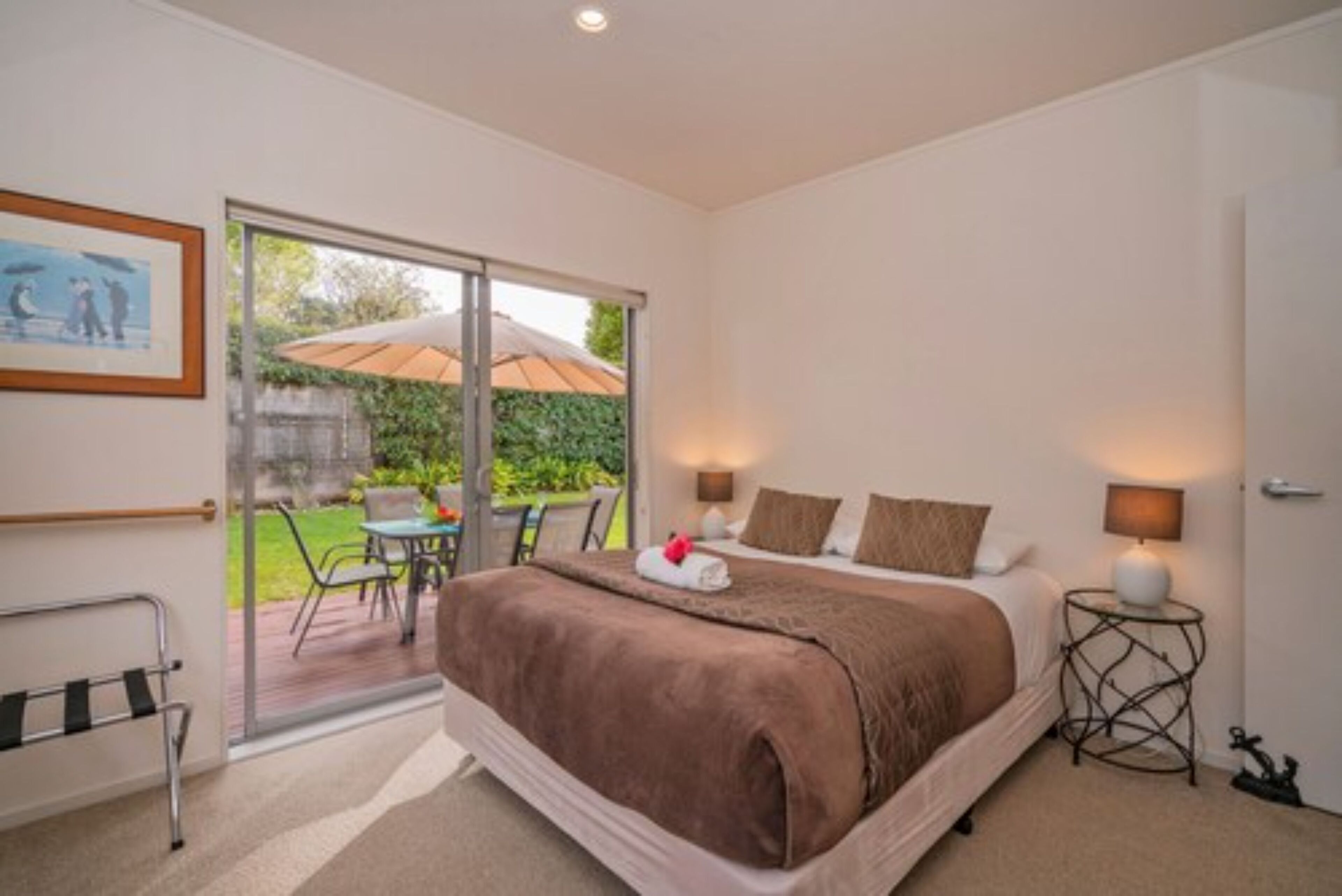 A bedroom with a large bed, a sliding glass door to a patio, a small table, and a chair.