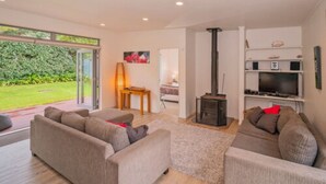 A modern living room with a fireplace, sofas, and a TV. - Tatahi Lodge Beach Resort (Hahei)
