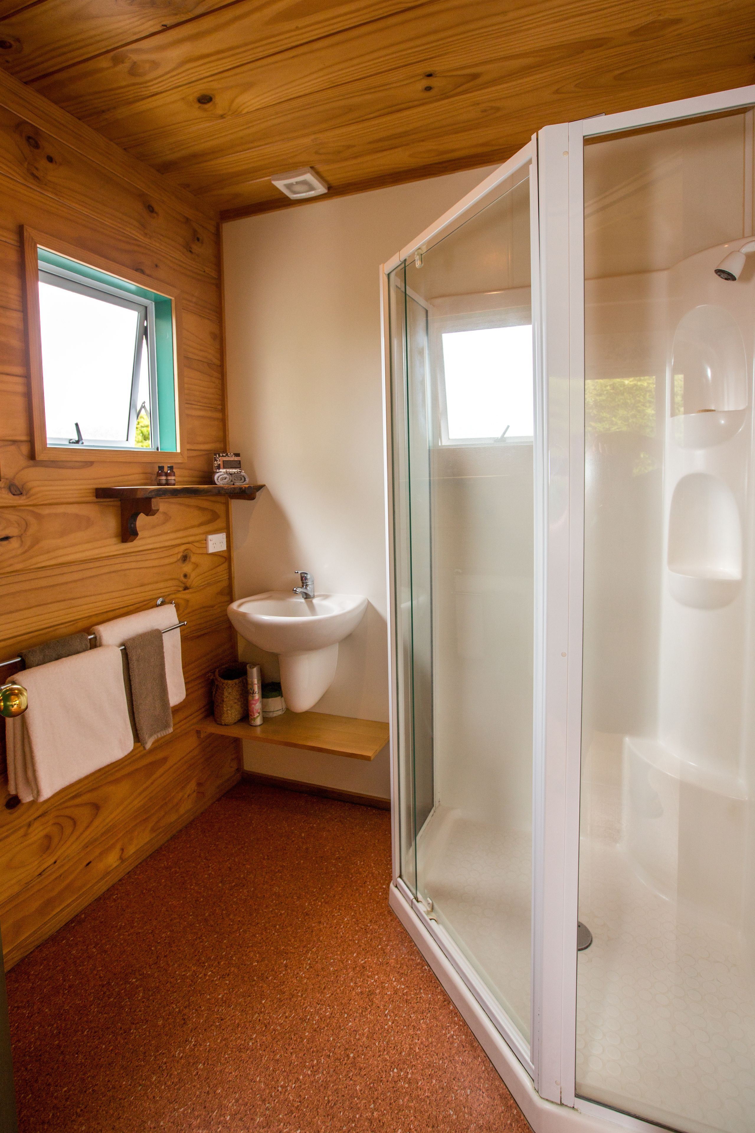 Een badkamer met houten wanden, een wastafel, een glazen douchecabine en een raam.