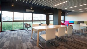 A modern conference room with a large table and chairs, large windows with a city view, and a ceiling with linear light fixtures. - Landmark Residence (Bang Sao Thong)