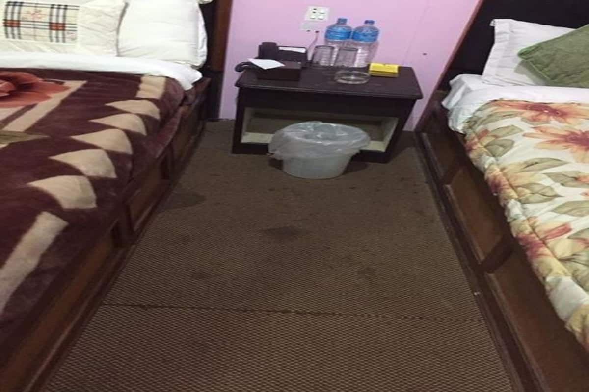 Ein schmales Hotelzimmer mit zwei Betten, einem kleinen Tisch und einem Mülleimer sowie einer Steckdose.