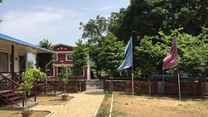 A courtyard with a gravel path, a red building with a blue roof, and two flags. - Regal Hetauda Resort Pvt. Ltd. (Hetauda)