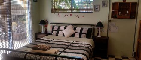 A bedroom with a bed, two nightstands, a window with blinds, a wall-mounted shelf, and a checkered floor.