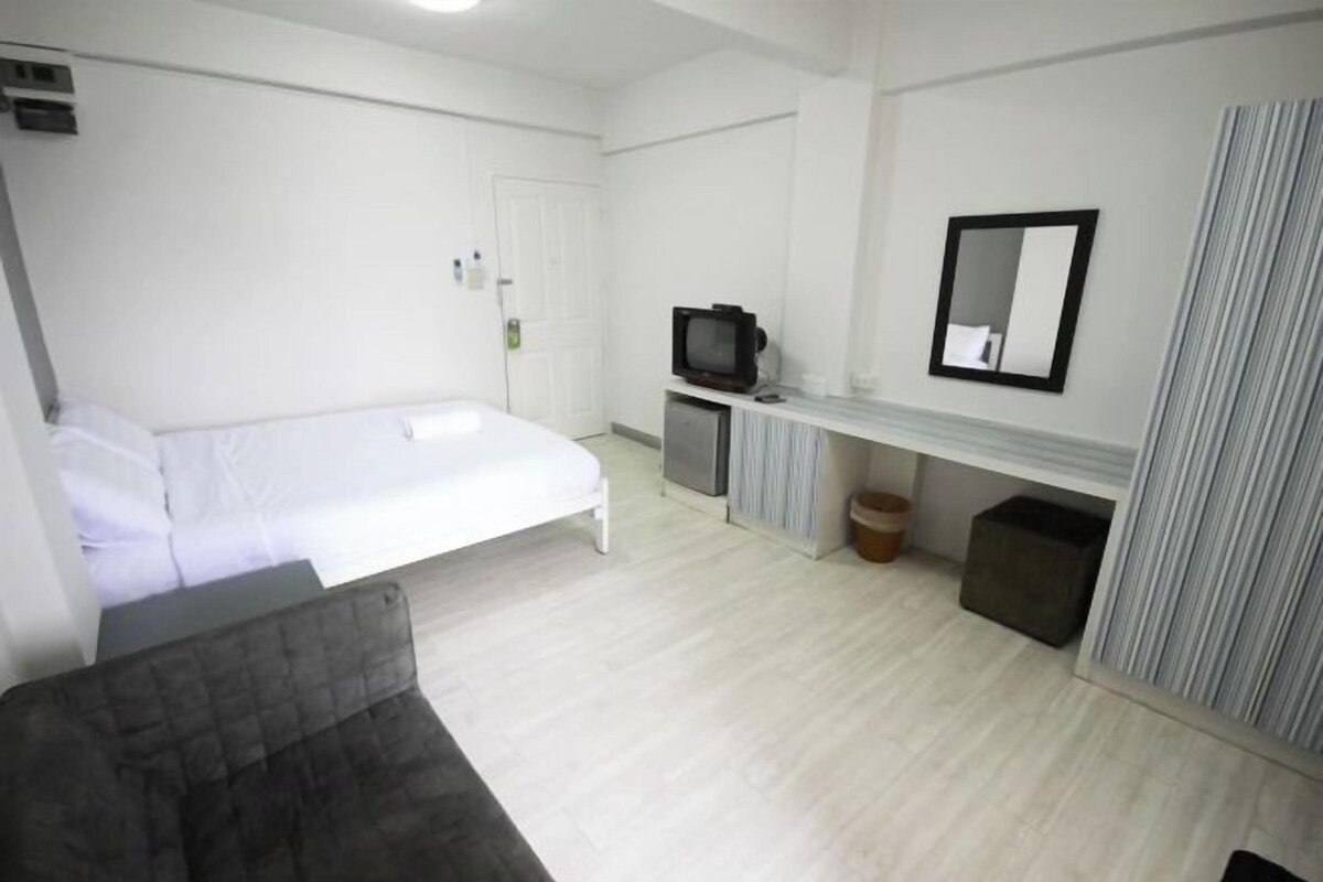 A bedroom with a bed, a television, a mirror, and a small cabinet.