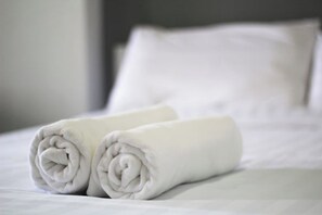 A neatly made bed with two rolled white towels placed on it. - Sakun Place (Samut Prakan)