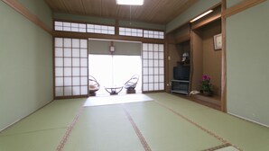 A traditional Japanese room with tatami flooring, a sliding door, and a television on a wooden shelf. - Tamagawa Ryokan (Tahara)
