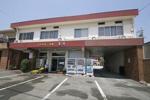 A building with a red and white facade, a covered entrance, vending machines, and potted plants. - Tamagawa Ryokan (Tahara)