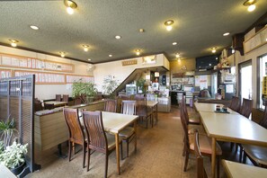 Un restaurante con muebles de madera, una zona de cocina y una escalera que sube a un nivel superior.
