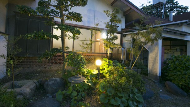 A residential garden with a well-maintained lawn, a variety of plants, and a stone pathway. - Tamagawa Ryokan (Tahara)
