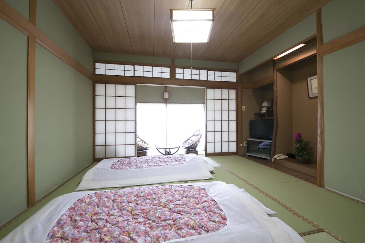 A traditional Japanese room with tatami flooring, two beds with floral bedding, a television, and a small table with chairs.