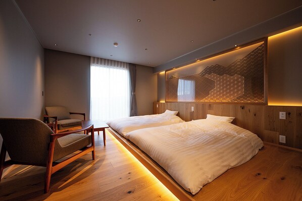 Una habitación de hotel moderna con piso de madera, una cama grande, un escritorio con silla y un ventanal con cortinas.