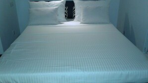 Uma cama de solteiro com roupa de cama branca num quarto com paredes lisas.