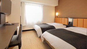 Ein Hotelzimmer mit zwei Betten, einem Schreibtisch, einem Fernseher und einem Fenster mit Vorhängen.