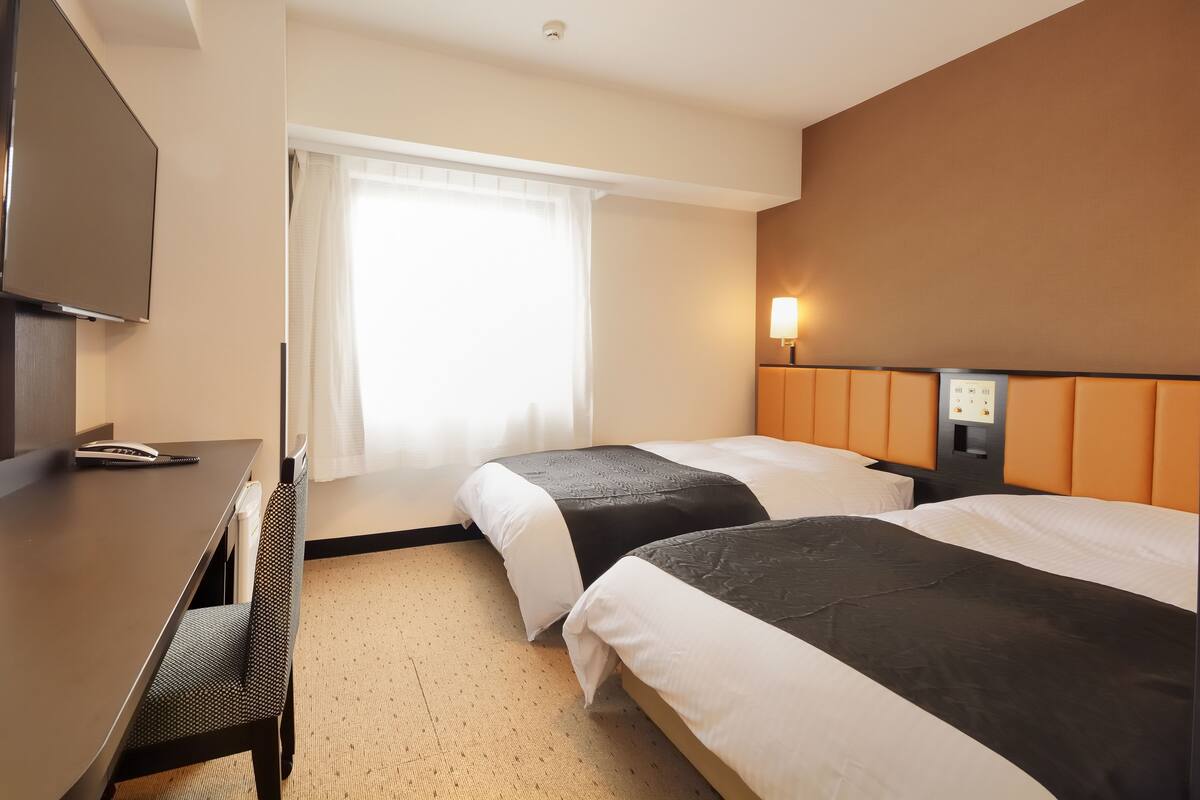 Une chambre d’hôtel avec deux lits, un bureau, une télévision et une fenêtre avec des rideaux.