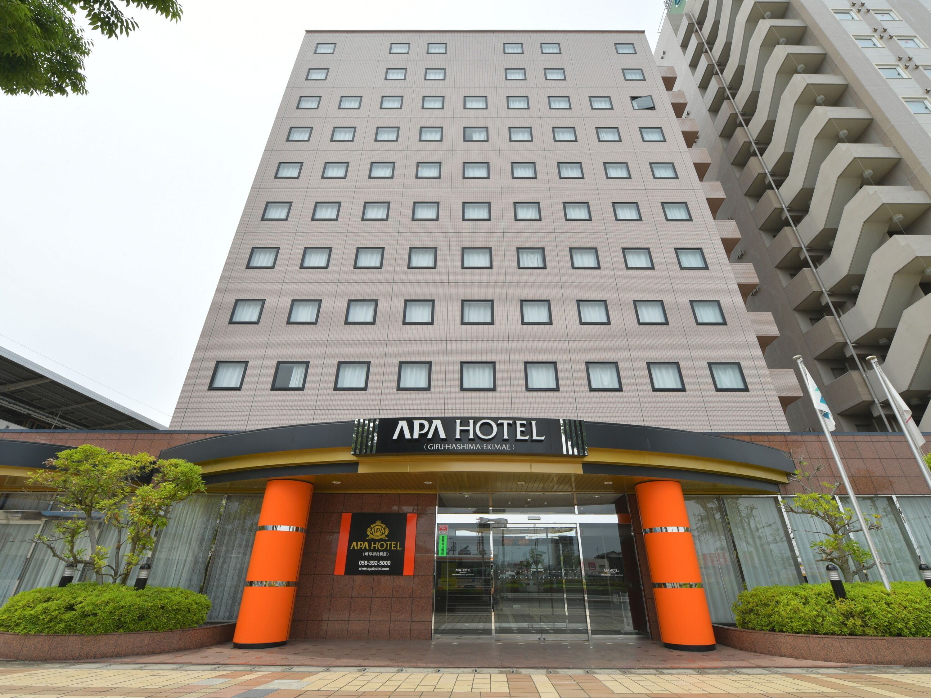 Un moderno edificio de hotel con una entrada destacada, ventanas amplias y un letrero que dice 'APA HOTEL'.