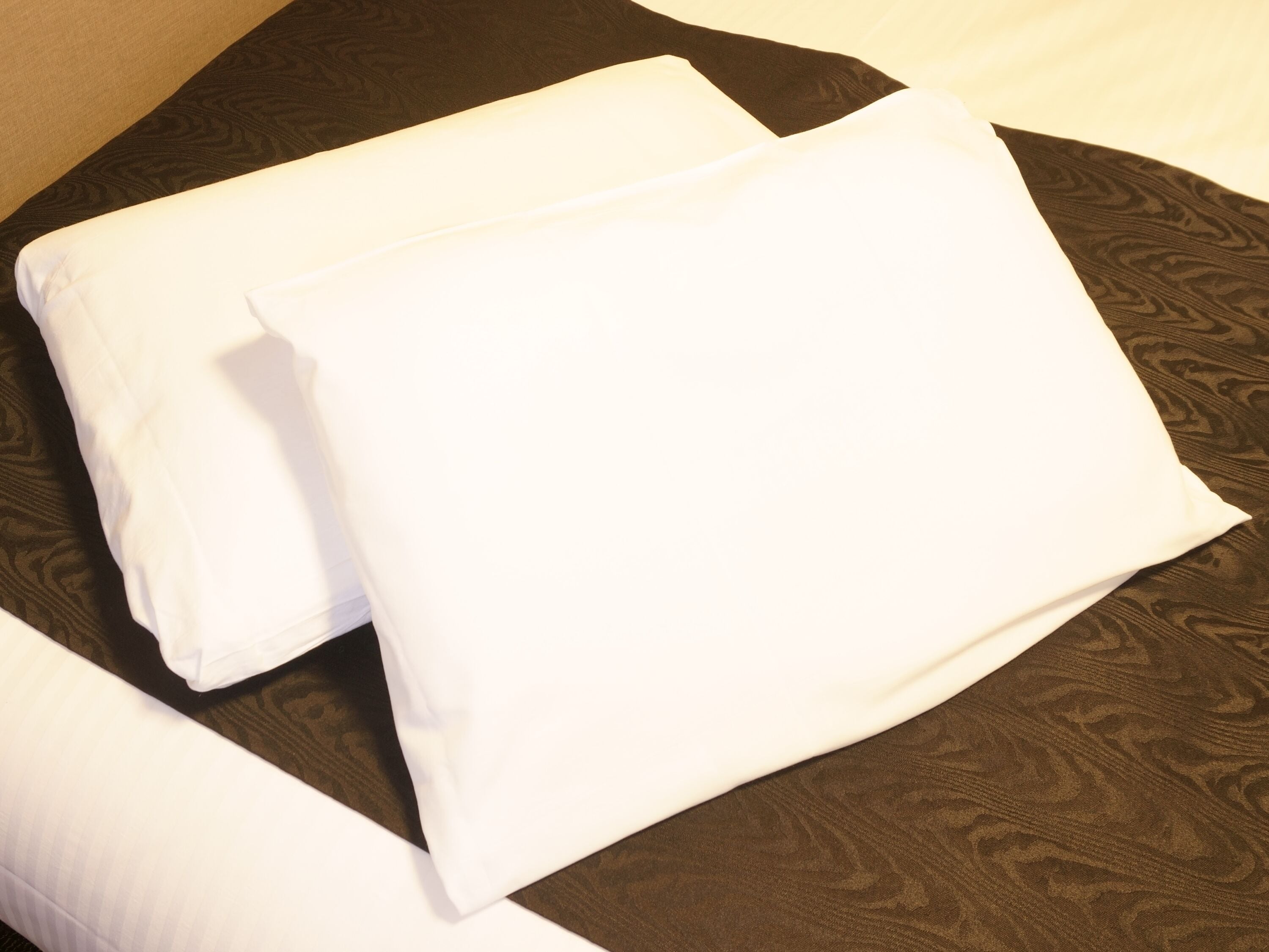 Two white pillows on a dark patterned bedspread.