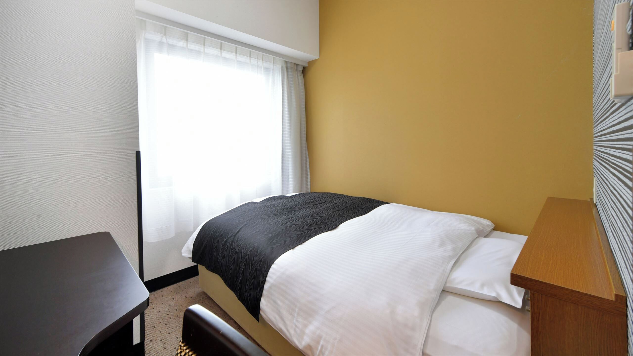Een hotelkamer met een bed, een bureau en een raam met gordijnen.