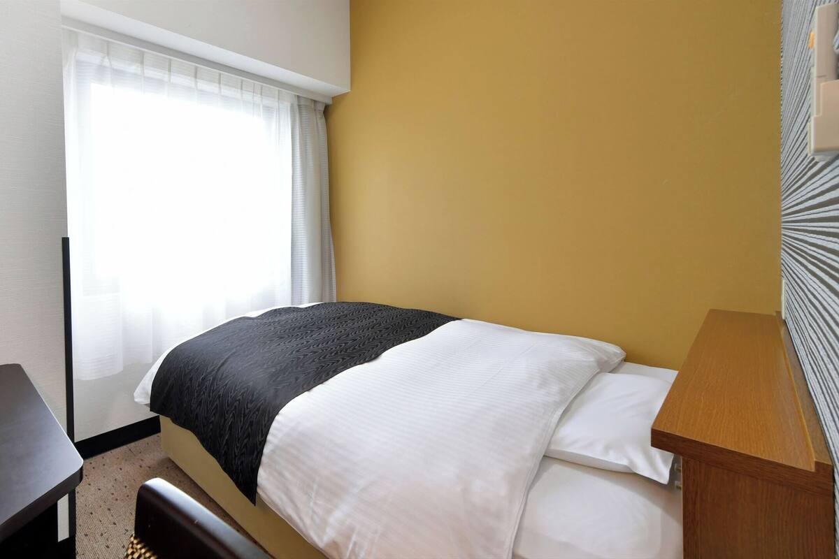Une chambre d’hôtel avec un lit, un bureau et une fenêtre avec des rideaux.