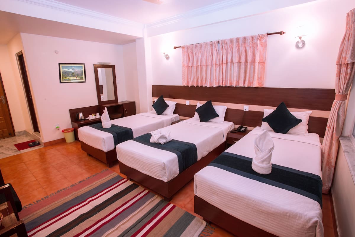 Habitación de hotel con cuatro camas, cabecera de madera, alfombra a rayas, una mesita con una lámpara y un cuadro en la pared.