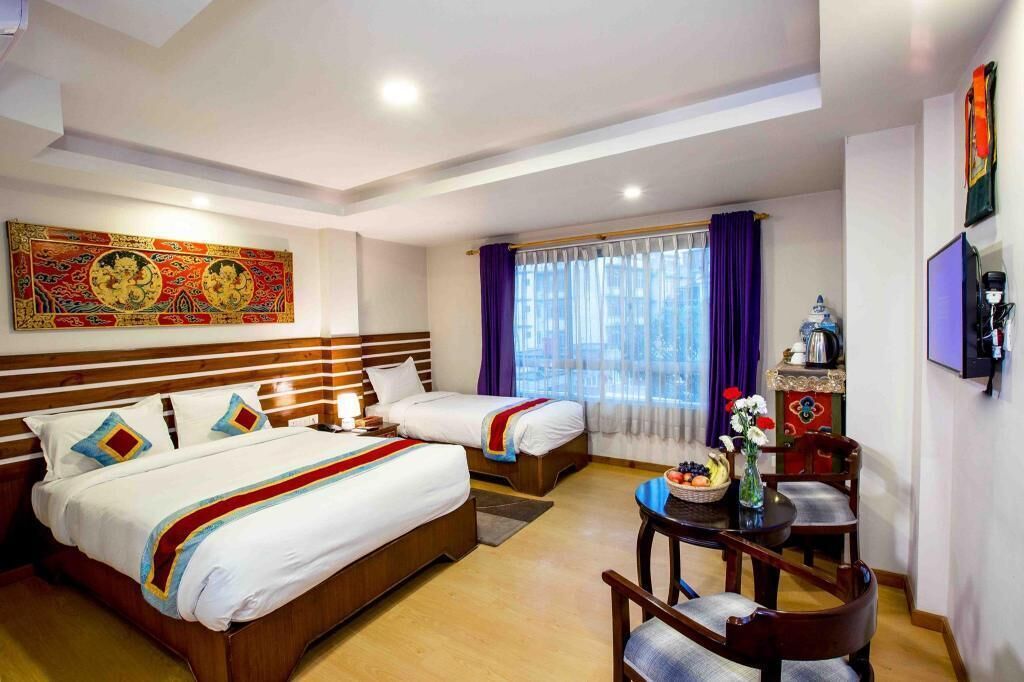 A hotel room with two beds, a dining table with chairs, a coffee machine, and a decorative vase.