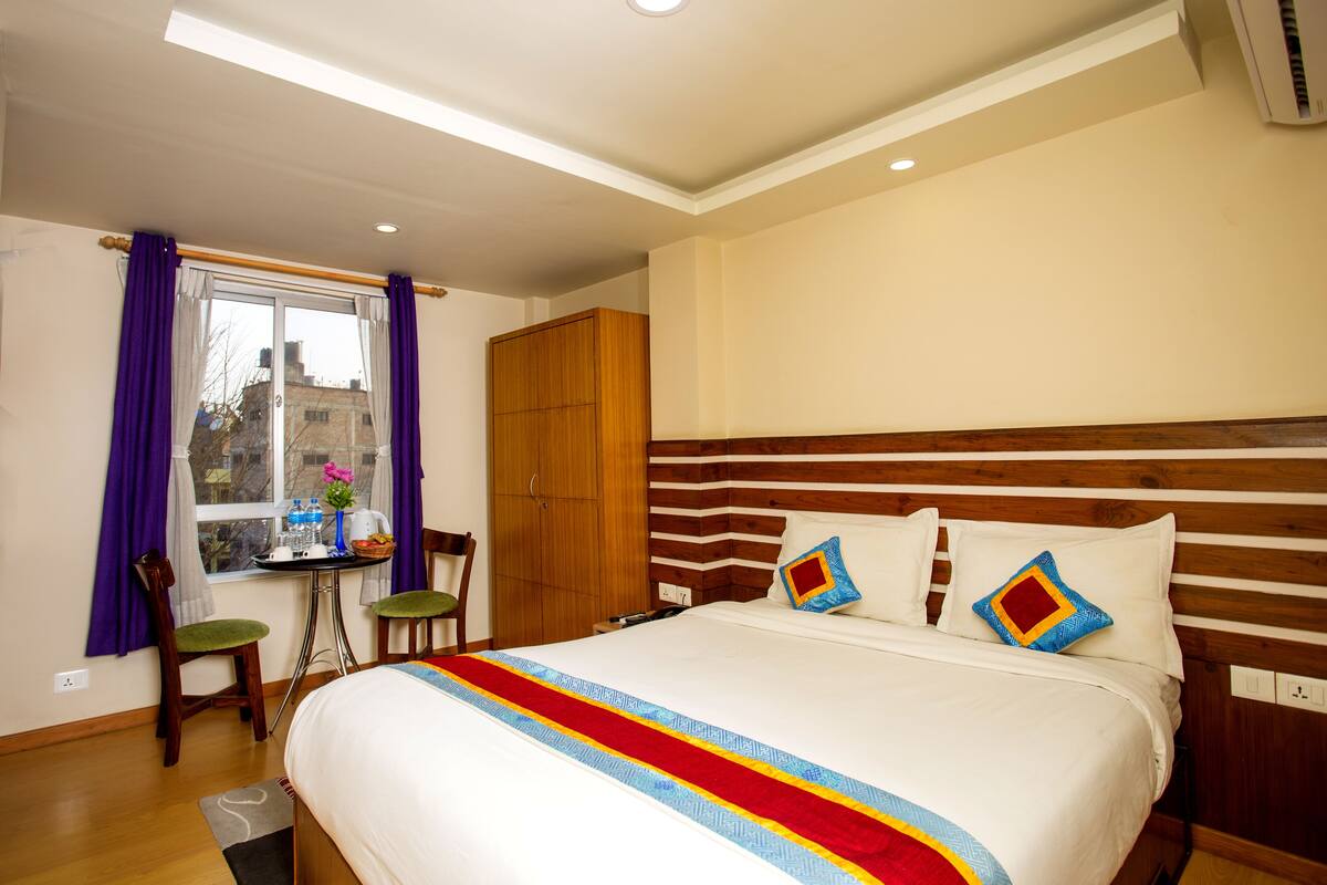 Una habitación de hotel con una cama grande, cabecero de madera y una ventana con cortinas moradas.
