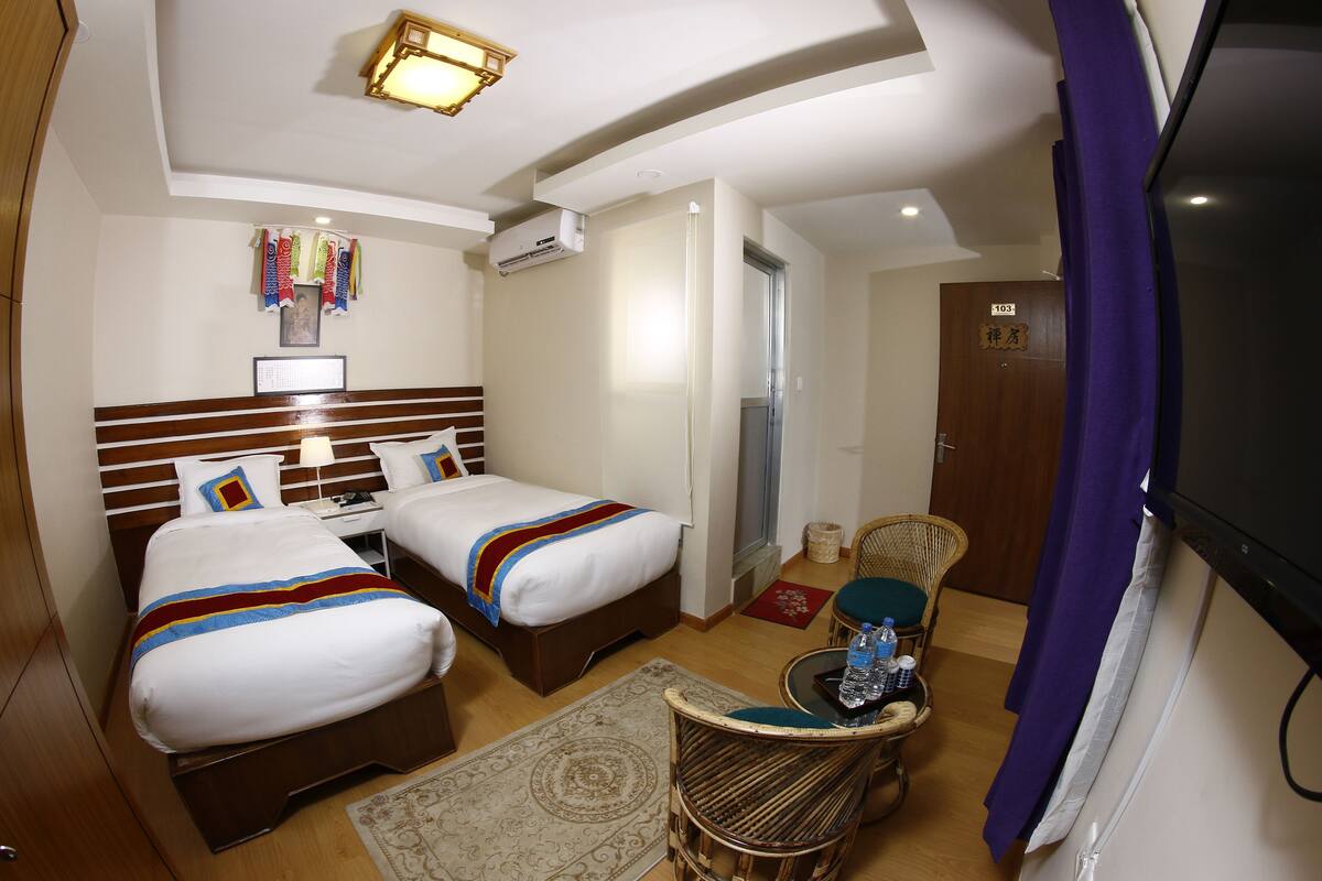 Habitación de hotel con dos camas, una mesita con una silla, un televisor y una puerta con el número 103.