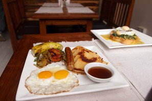Una mesa de comedor con un plato de comida que incluye huevos, un plátano y una salchicha.