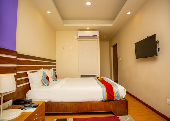 Una habitación de hotel con una cama de madera, un televisor en la pared y un equipo de aire acondicionado.