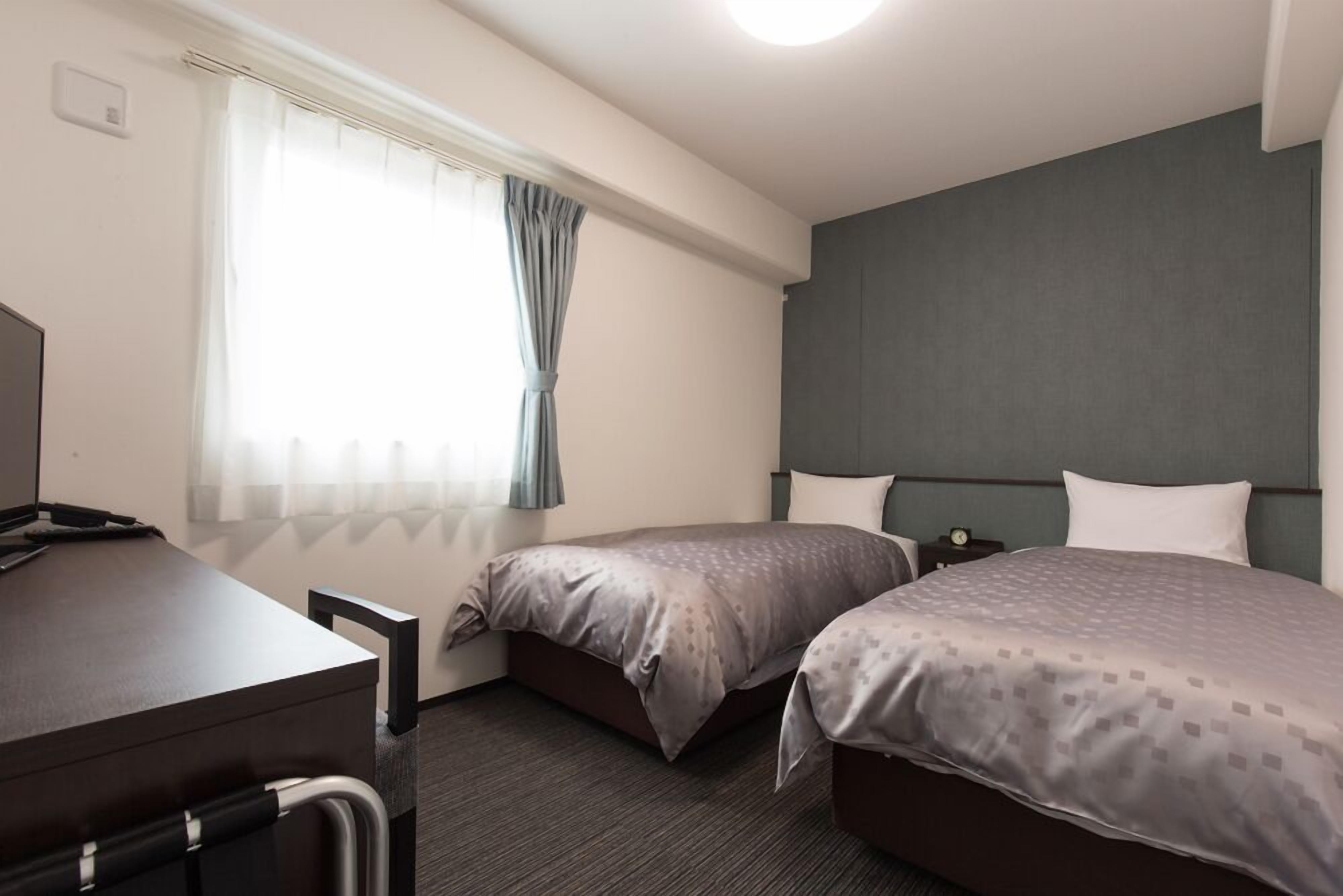 Une chambre d’hôtel avec deux lits, un bureau et une fenêtre avec des rideaux.