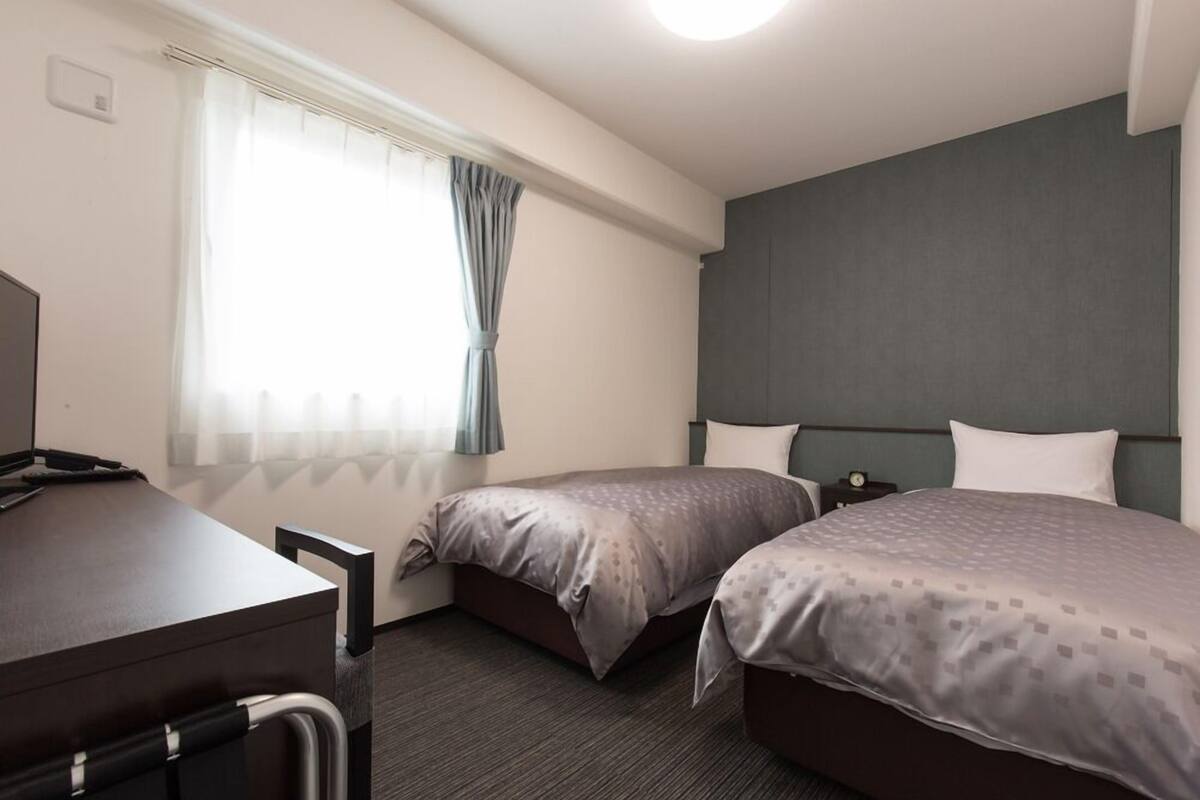A hotel room with two beds, a desk, and a window with curtains.