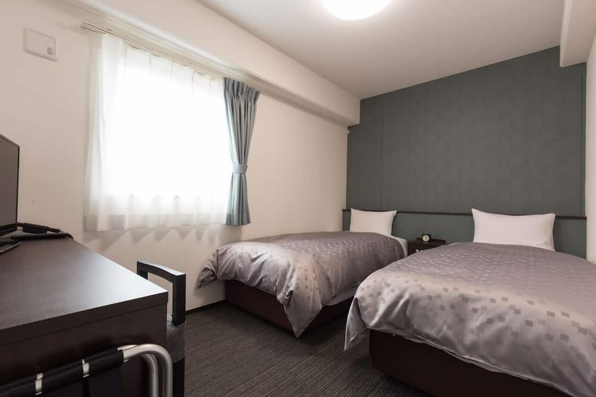 Une chambre d’hôtel avec deux lits, un bureau et une fenêtre avec des rideaux.