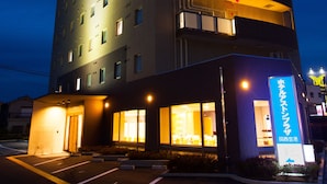 Un hôtel à plusieurs étages, dot é d’un design moderne, avec une façade incurvée, des fenêtres illuminées et une entrée bien visible, agrémentée d’une enseigne.
