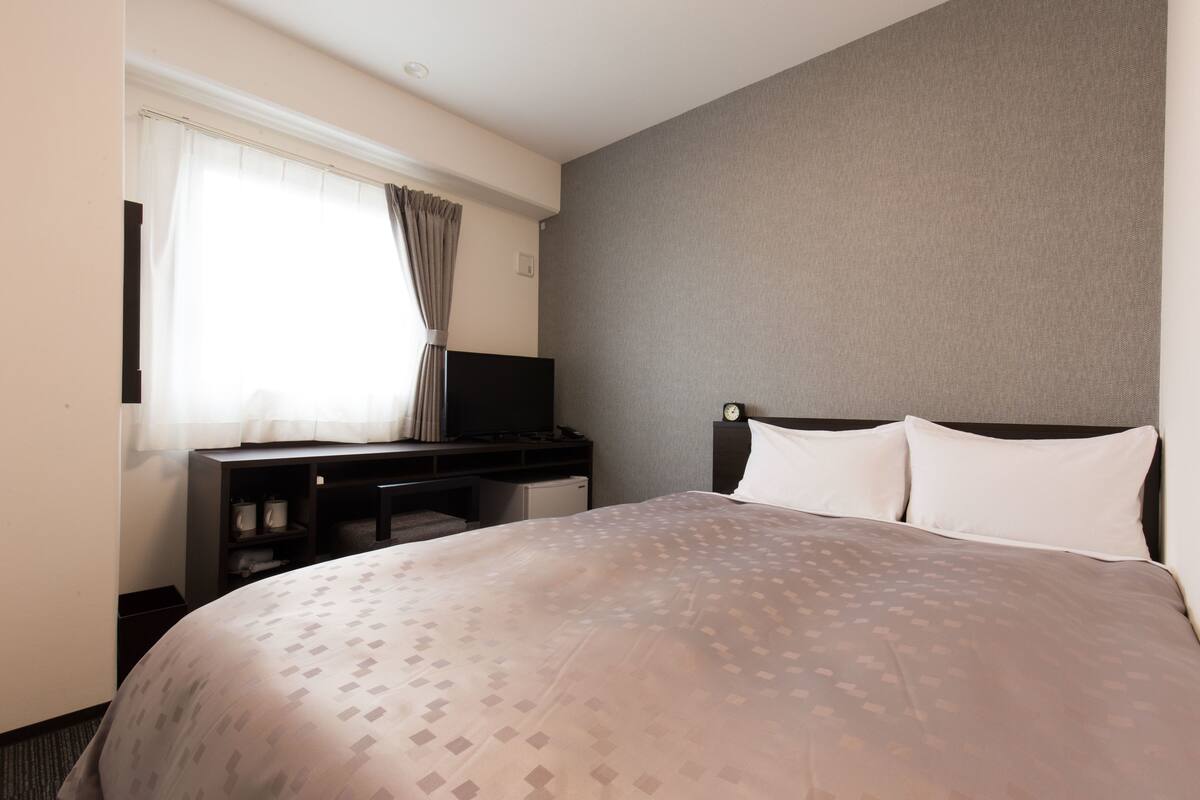 Ein Hotelzimmer mit einem Bett, einem Schreibtisch mit Fernseher und einem Fenster mit Vorhängen.