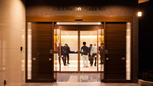 L’entrée de l’hôtel Aston Plaza KIX se distingue par son design moderne, avec une façade en bois et des portes en verre.