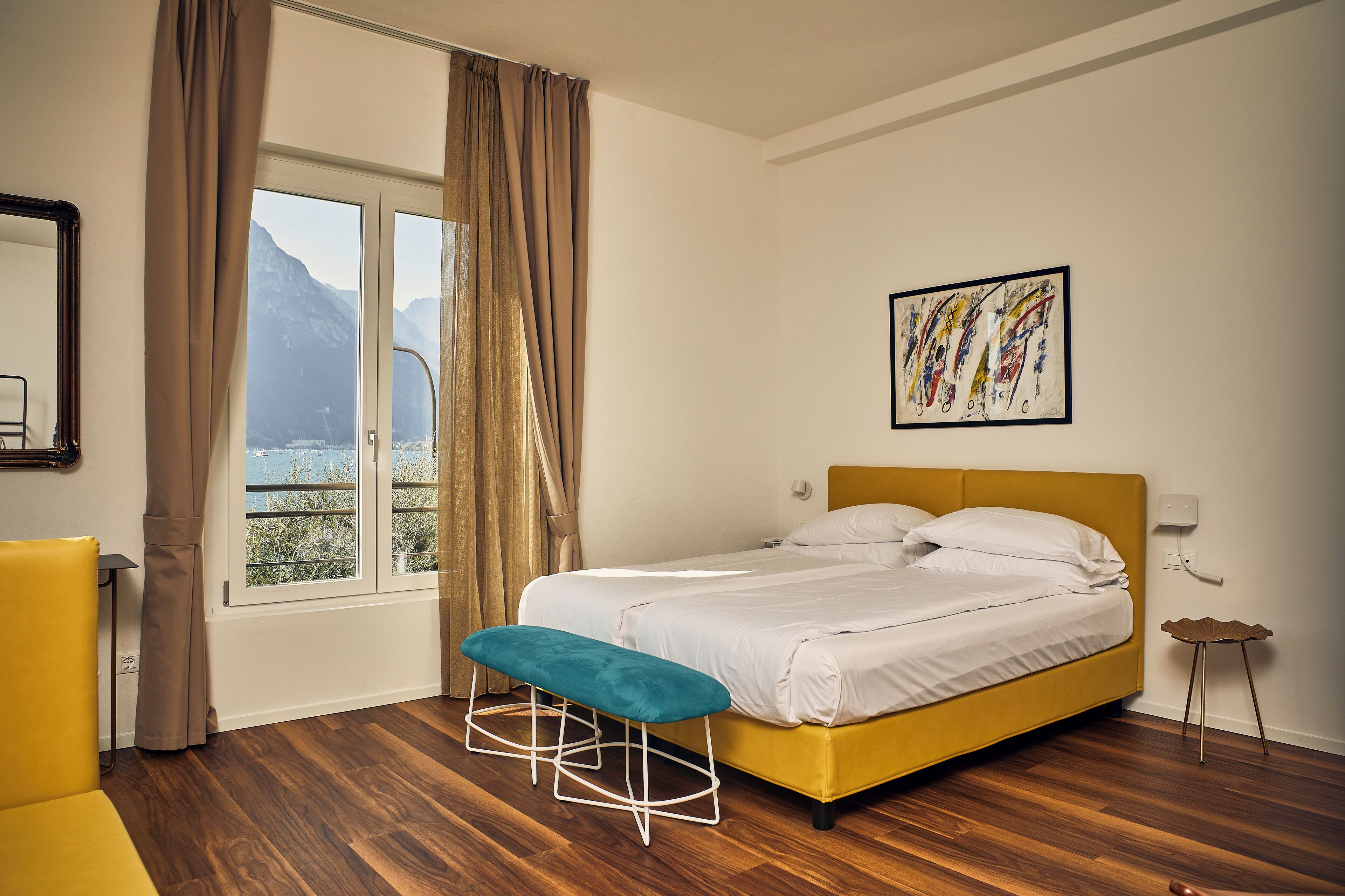 Un dormitorio con cama, un banco, una ventana con cortinas, un cuadro y vistas a montañas.